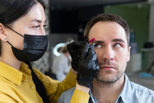 Jeune homme sur la procédure de correction des sourcils dans un salon de beauté. Maître femme enlève un cil d'un gars. épiler les sourcils des hommes.