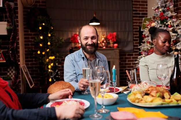 Jeune homme profitant d'un dîner de Noël festif avec diverses personnes se réunissant avec sa famille autour de la table pour la veille de Noël Diverses personnes s'amusant pendant la célébration de la saison hivernale décor confortable
