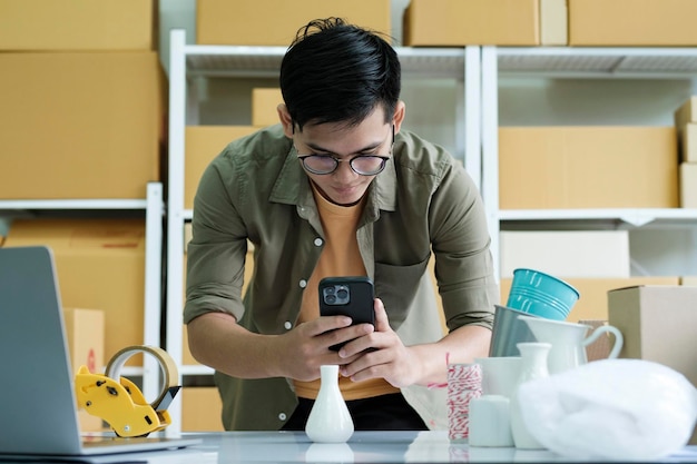 Photo jeune homme propriétaire d'une entreprise en ligne à l'aide d'un téléphone portable vérifiant la boîte de colis