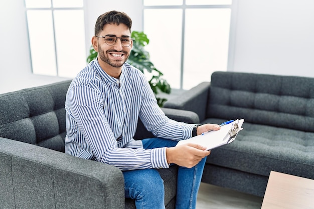 Jeune homme psychologue au bureau de consultation avec un sourire heureux et cool sur le visage. personne chanceuse.