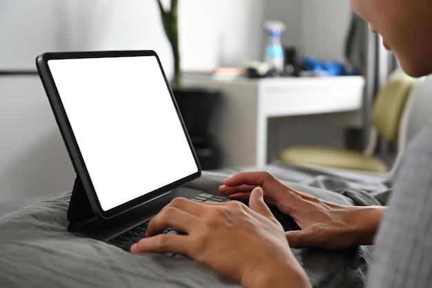 Jeune homme en pyjama naviguant sur Internet avec une tablette informatique sur son lit