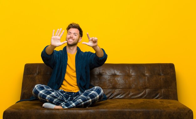 Jeune homme en pyjama souriant et amical, montrant le numéro sept ou sept avec la main en avant, comptant à rebours