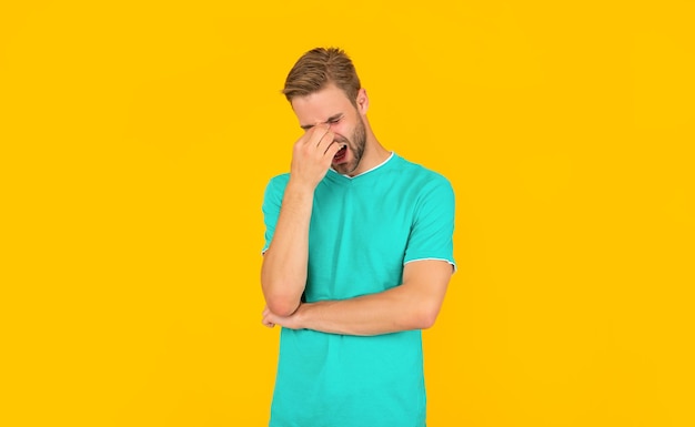 Le jeune homme qui crie a mal à la tête sur fond jaune. soin des cheveux et de la barbe. mec non rasé confiant et beau. mode décontractée masculine. beauté des hommes. portrait d'homme à poils en chemise bleue.