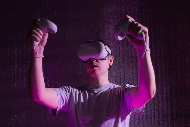 Jeune homme de race blanche de 25 à 30 ans utilisant un casque de réalité virtuelle. VR, avenir, gadgets, concept technologique en néon.