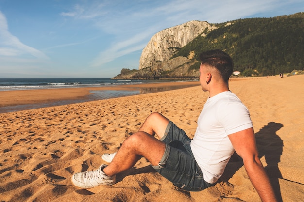 Photo jeune homme de race blanche assis sur le sable d'une plage basque.