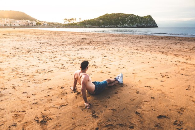 Photo jeune homme de race blanche assis sur le sable d'une plage basque.