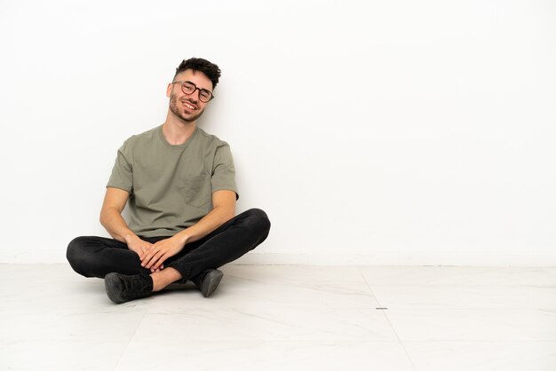 Jeune homme de race blanche assis sur le sol isolé sur fond blanc avec les bras croisés et avec impatience