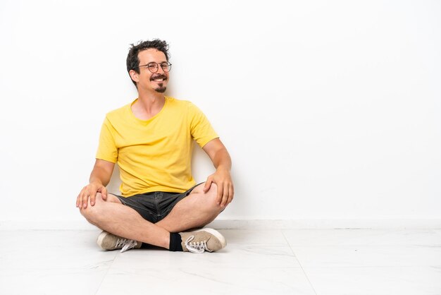 Jeune homme de race blanche assis sur le sol isolé sur fond blanc avec les bras croisés et avec impatience