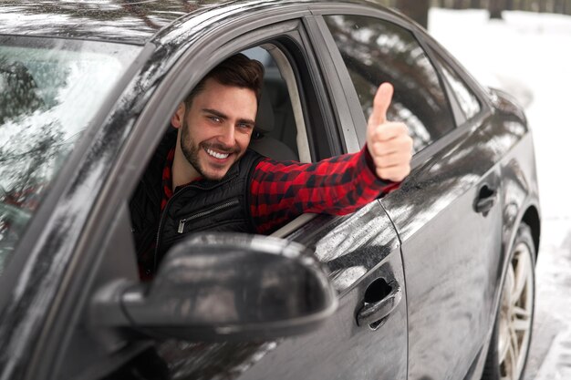 Jeune homme de race blanche attrayant est assis au volant de sa voiture journée d'hiver ensoleillée