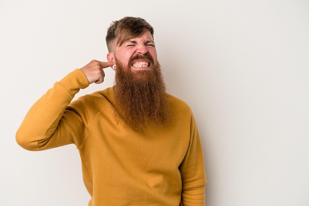 Jeune homme de race blanche au gingembre avec une longue barbe isolé sur fond blanc couvrant les oreilles avec les mains.