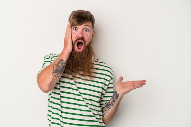 Jeune homme de race blanche au gingembre avec une longue barbe isolé sur fond blanc impressionné tenant l'espace de copie sur la paume.