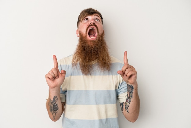 Jeune homme de race blanche au gingembre avec une longue barbe isolé sur fond blanc pointant vers le haut avec la bouche ouverte.