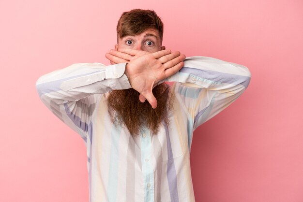 Jeune homme de race blanche au gingembre avec une longue barbe isolé sur fond rose faisant un geste de déni