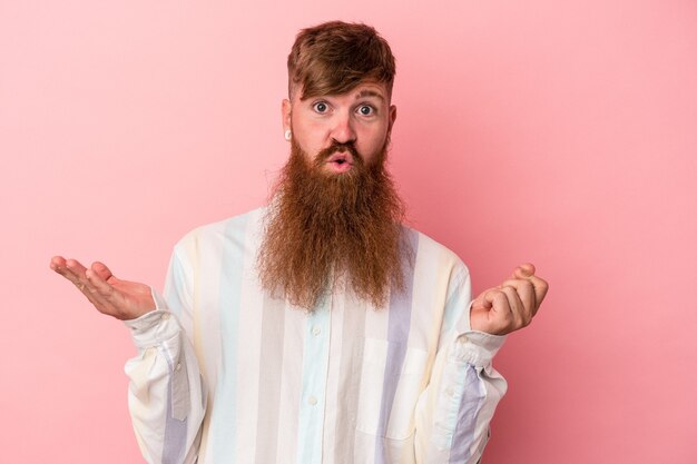 Jeune homme de race blanche au gingembre avec une longue barbe isolé sur fond rose montrant qu'elle n'a pas d'argent.