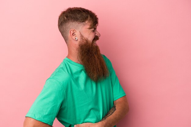 Jeune homme de race blanche au gingembre avec une longue barbe isolé sur fond rose souffrant d'un mal de dos.