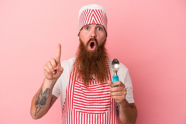 Jeune homme de race blanche au gingembre avec une longue barbe tenant une boule isolée sur fond rose ayant une bonne idée, concept de créativité.