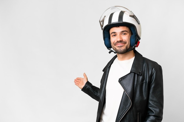 Jeune homme de race blanche avec un casque de moto sur fond blanc isolé tendant les mains sur le côté pour inviter à venir