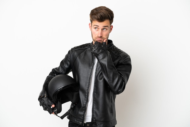 Jeune homme de race blanche avec un casque de moto isolé sur fond blanc ayant des doutes et pensant