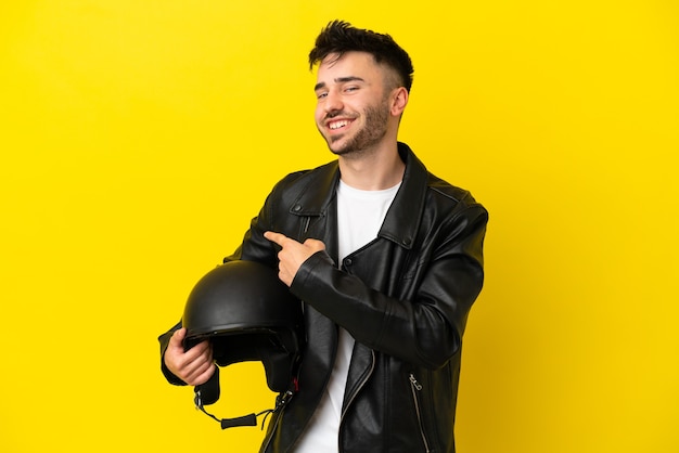 Jeune homme de race blanche avec un casque de moto isolé sur fond jaune pointant vers l'arrière