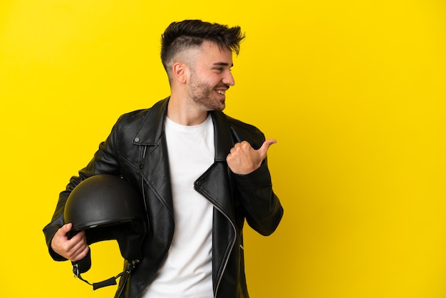 Jeune homme de race blanche avec un casque de moto isolé sur fond jaune pointant vers le côté pour présenter un produit