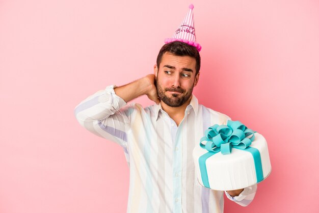 Jeune homme de race blanche célébrant son anniversaire isolé sur un mur rose touchant l'arrière de la tête, en pensant et en faisant un choix