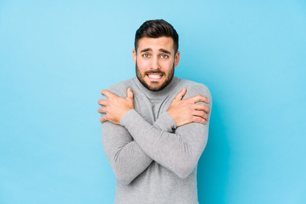 Jeune homme de race blanche contre un mur bleu isolé qui devient froid en raison d'une basse température ou d'une maladie.