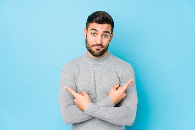 Jeune homme de race blanche contre un mur bleu, des points isolés sur le côté, essaie de choisir entre deux options.