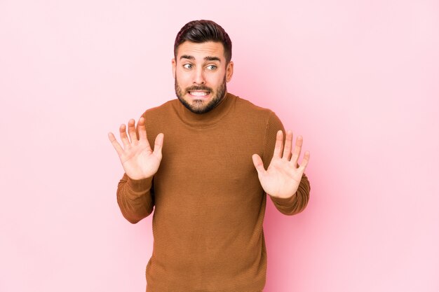 Jeune homme de race blanche contre un mur rose rejetant quelqu'un montrant un geste de dégoût.