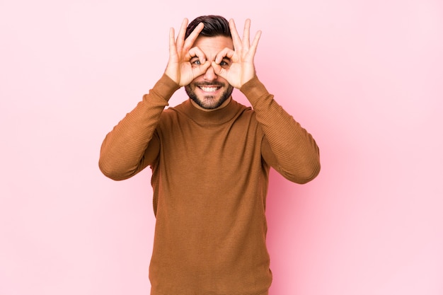 Jeune homme de race blanche contre un rose isolé montrant signe correct sur les yeux