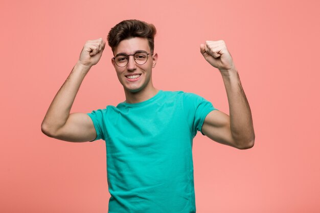 Jeune homme de race blanche cool célébrant une journée spéciale, saute et lève les bras avec énergie.