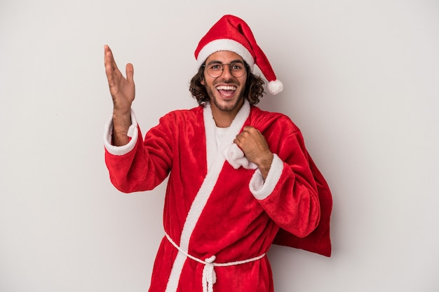 Jeune homme de race blanche déguisé en père noël isolé sur fond gris recevant une agréable surprise, excité et levant les mains.