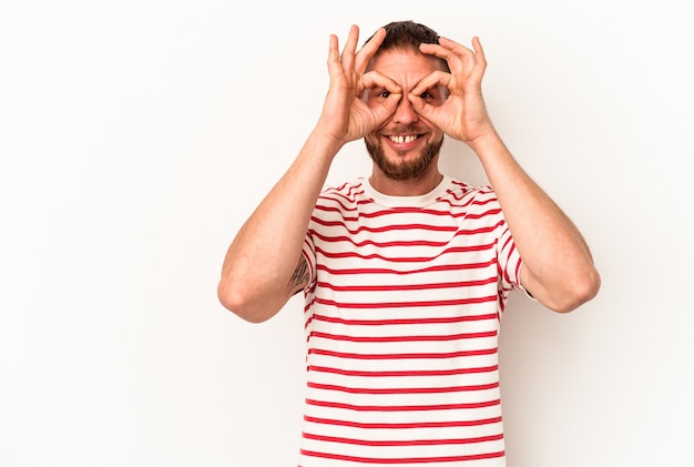 Jeune homme de race blanche avec diastème isolé sur fond blanc excité en gardant le geste ok sur les yeux.