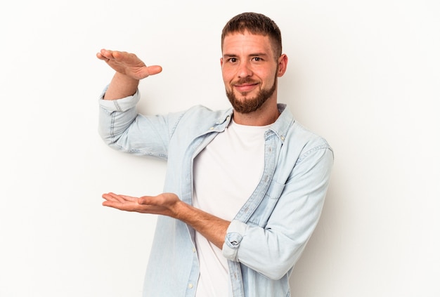 Jeune homme de race blanche avec diastème isolé sur fond blanc tenant quelque chose de petit avec les index, souriant et confiant.