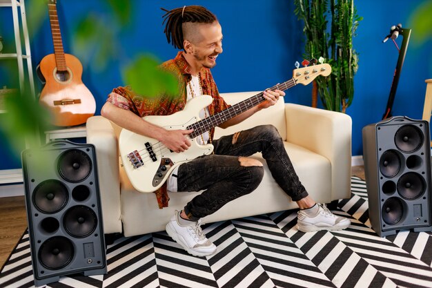 Jeune homme de race blanche avec des dreadlocks jouant de la guitare électrique dans sa chambre