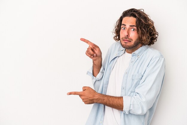 Jeune homme de race blanche isolé sur fond blanc choqué pointant avec l'index vers un espace de copie.