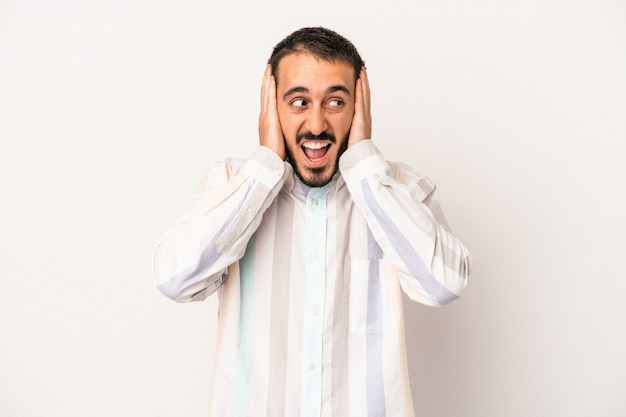 Jeune homme de race blanche isolé sur fond blanc couvrant les oreilles avec les mains en essayant de ne pas entendre un son trop fort.