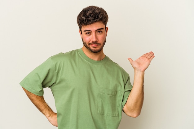 Jeune homme de race blanche isolé sur fond blanc doutant et haussant les épaules dans un geste de questionnement.