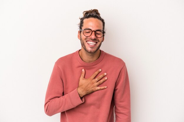 Jeune homme de race blanche isolé sur fond blanc éclate de rire en gardant la main sur la poitrine.