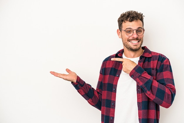 Jeune homme de race blanche isolé sur fond blanc excité tenant un espace de copie sur la paume.