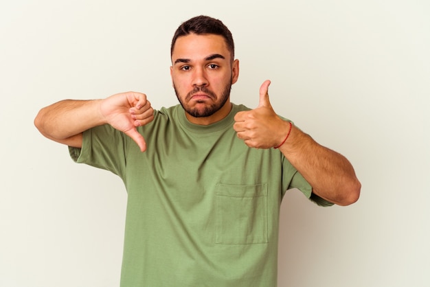 Jeune homme de race blanche isolé sur fond blanc montrant les pouces vers le haut et les pouces vers le bas, difficile de choisir le concept