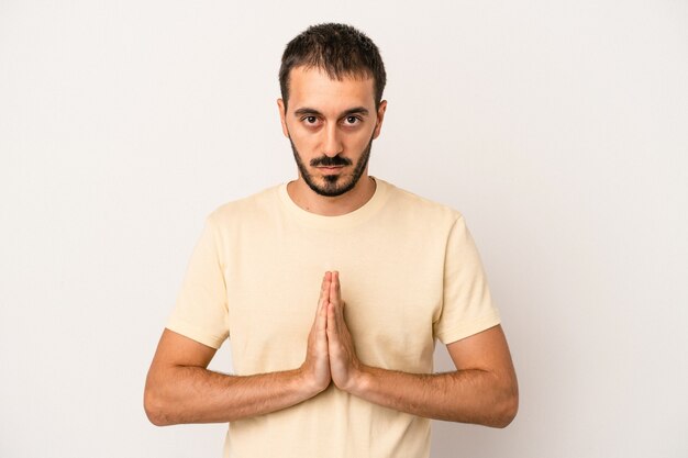 Jeune homme de race blanche isolé sur fond blanc priant, montrant la dévotion, personne religieuse à la recherche d'inspiration divine.