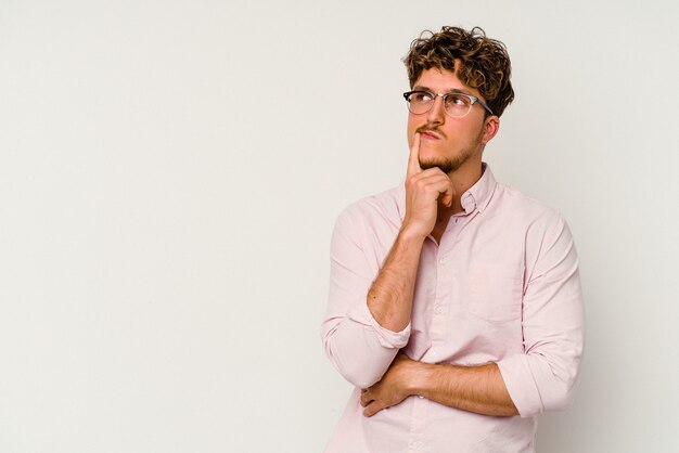 Jeune homme de race blanche isolé sur fond blanc regardant de côté avec une expression douteuse et sceptique.