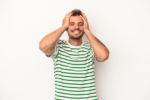 Jeune homme de race blanche isolé sur fond blanc rit joyeusement en gardant les mains sur la tête. Notion de bonheur.