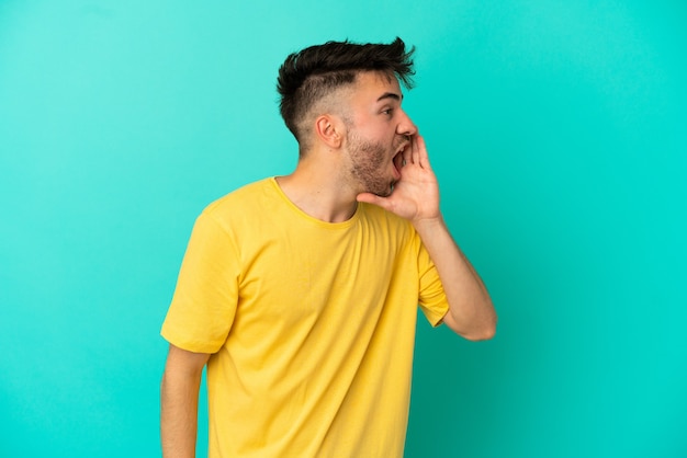 Jeune homme de race blanche isolé sur fond bleu criant avec la bouche grande ouverte sur le côté