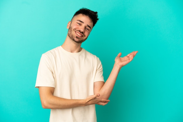 Jeune homme de race blanche isolé sur fond bleu étendant les mains sur le côté pour inviter à venir