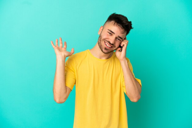 Jeune homme de race blanche isolé sur fond bleu en gardant une conversation avec le téléphone portable avec quelqu'un