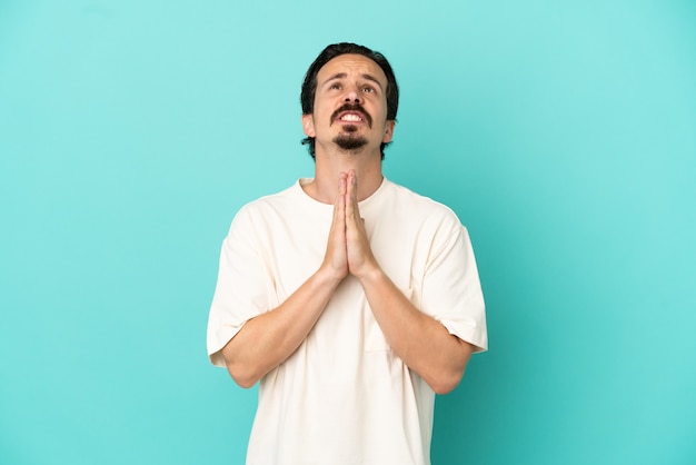 Jeune homme de race blanche isolé sur fond bleu maintient la paume ensemble. La personne demande quelque chose