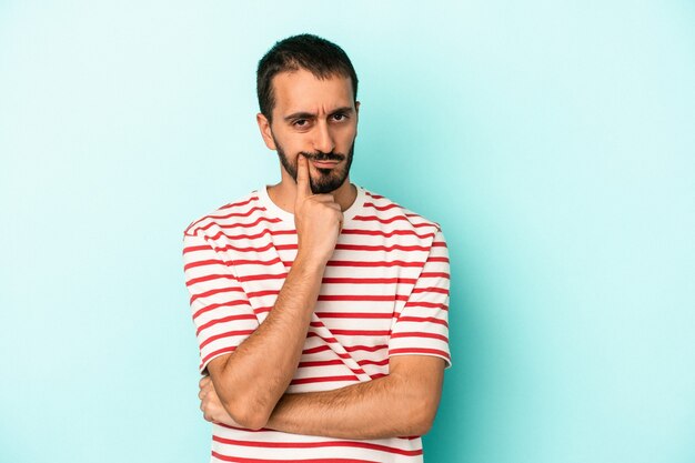 Jeune homme de race blanche isolé sur fond bleu malheureux à la recherche à huis clos avec une expression sarcastique.