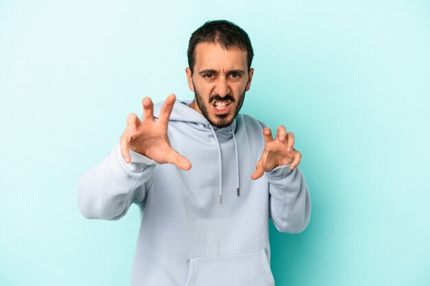 Jeune homme de race blanche isolé sur fond bleu montrant des griffes imitant un chat, geste agressif.