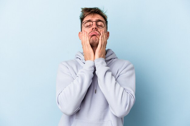 Jeune homme de race blanche isolé sur fond bleu pleurnichant et pleurant de manière inconsolable.